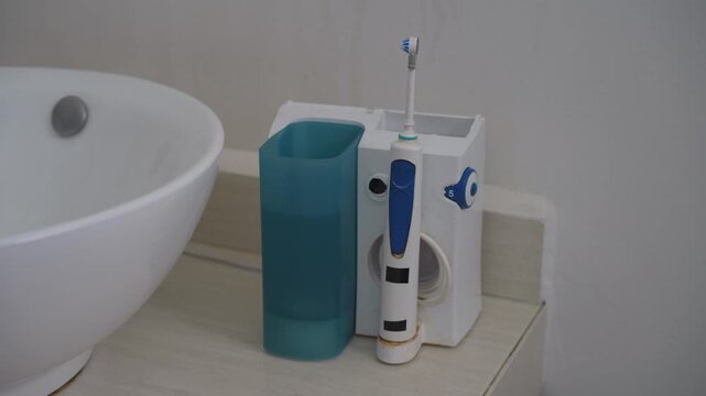 Dental water flosser working on a table near a bathroom sink with splashing water and pump sound. Uncompressed 24 bit audio. Oral hygiene technology, personal care and dental health concept.