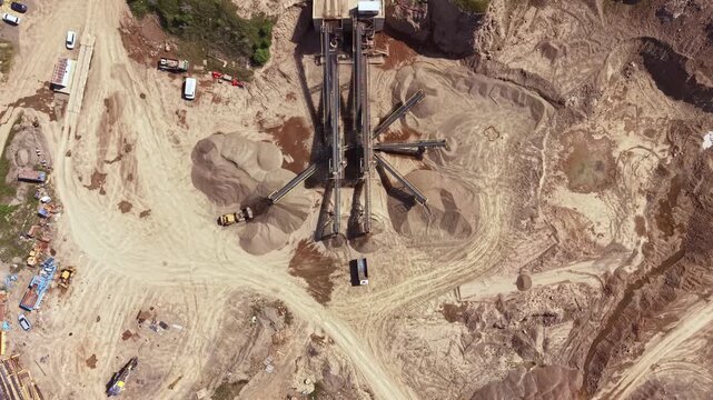 Heavy machinery moves and sorts sand and gravel at a construction site. Workers are present as vehicles transport materials across the site.