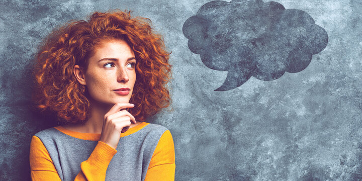 Thinking redhead woman looking at empty thought bubble on gray wall