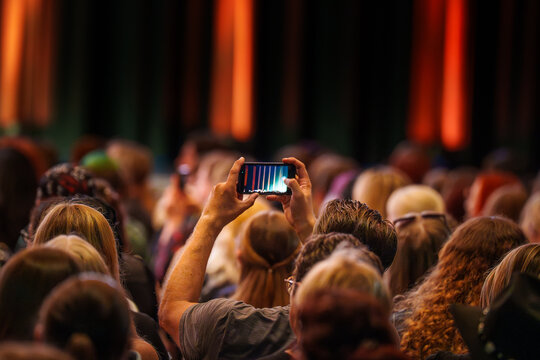 Audience person holding smartphone horizontal recording stage lights concert event