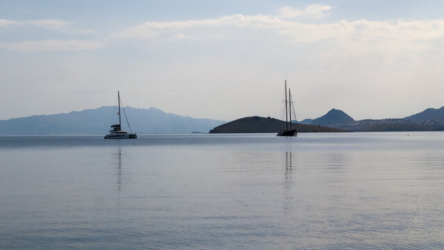 Sailing yachts on calm Aegean Sea in Bitez Bay, Bodrum, Turkey, with mountains and coastal landscape