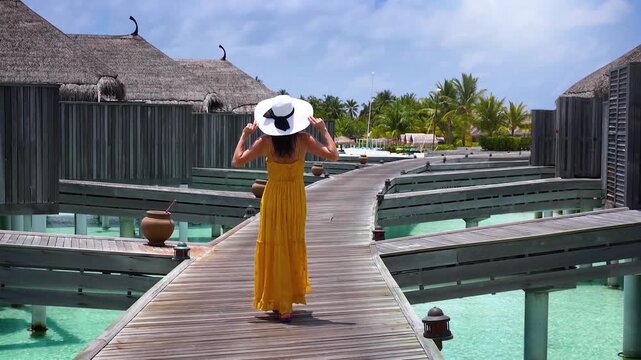 A elegant tourist woman with a yellow summer dress walks in the Maldives islands during her holiday time, tropical travel concept