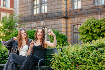 Fototapeta premium Two happy young women taking selfie on park bench outdoors in city