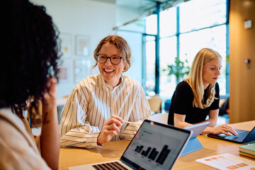 Diverse businesswomen collaborating and having a discussion in a bright office, working on laptops and tablets © we.bond.creations