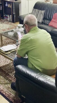 Viejo pensionista usando m&oacute;vil smartphone y jubilado consultando tel&eacute;fono celular tercera edad sentado con gafas y aud&iacute;fono en sof&aacute; sal&oacute;n de casa con pantalla tecnolog&iacute;a