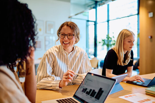 Diverse businesswomen collaborating and having a discussion in a bright office, working on laptops and tablets