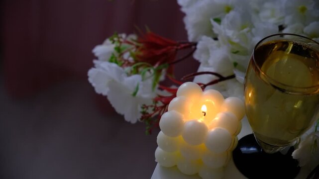 Cozy room, a burning candle casts a warm light on a bouquet of pristine white flowers, flute of champagne. Fairy lights twinkle softly, adding a touch of magic to the serene scene. Moment of quiet