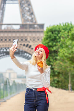 Woman taking selfie with croissant near Eiffel Tower in Paris travel lifestyle scene