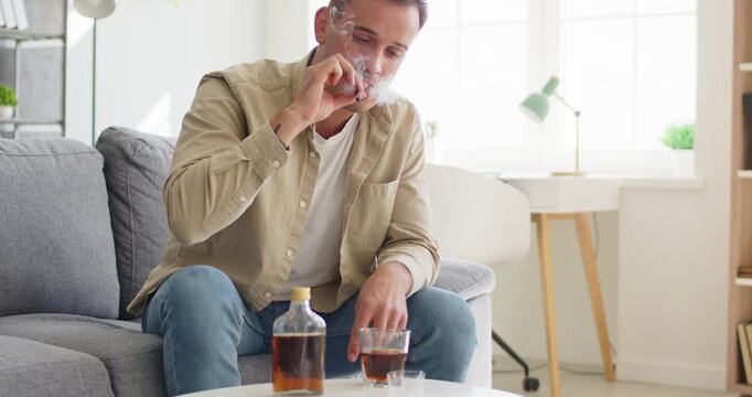 Man with whiskey alcohol bottle shows addiction. He holds a drink at home, reflecting stress, depression and loneliness linked to alcoholism and dependence. Clear concept of alcohol dependency.
