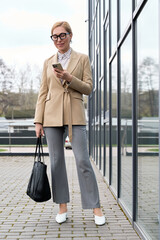 Elegant woman in stylish attire checking her phone outside a modern building