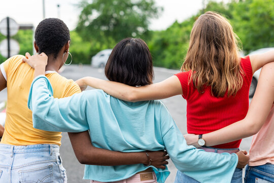 Group of diverse women with arms around each other outdoors.
