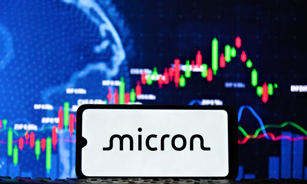 Micron Technology (MU) logo on a smartphone screen with a stock market chart in the background. Micron Technology is an American producer of computer memory and computer data storage.