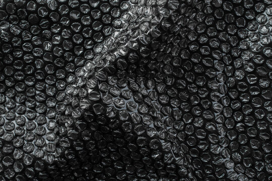 Black bubble wrap surface with heavy crumple texture, abstract packaging background