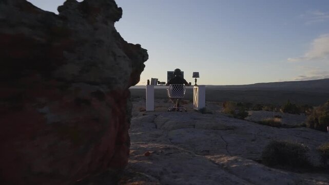 Person Sitting at Computer Desk on Desert Rocks During Sunset Slow Motion