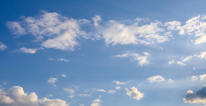 Light white and fluffy clouds float across a bright blue spring sky. Sunlight gently illuminates the edges of the cloudlets, creating volume and contrast in the heights.
