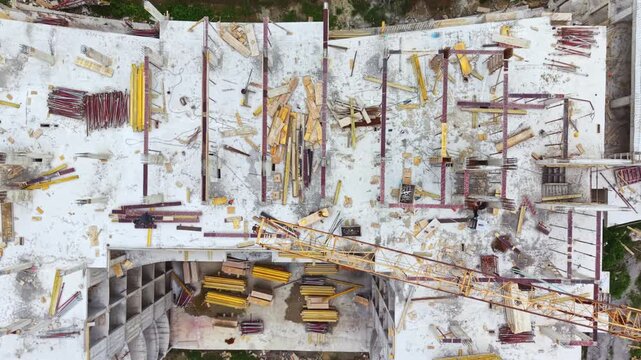 Aerial construction rooftop rusted cranes yellow vehicles showing derelict concrete slab, scattered rebar, parked excavators, overgrown vegetation creeping into