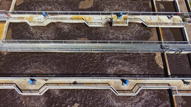 Aerial drone view industrial treatment basins showing rectangular sedimentation ponds with foamy surface, concrete walkways, rust stains, monitoring platforms,