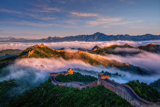 A breathtaking sunrise over the Jinshanling section of the Great Wall of China, with a sea of clouds rolling over the mountainous terrain.