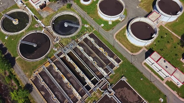 Aerial view sewage treatment plant showing circular clarifiers and rectangular aeration basins, access roads, control buildings and grassy buffers drone