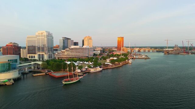 Norfolk, Virginia, beautiful 4K aerial drone video flying over the Elizabeth River toward Town Point Park during a sunset festival, showcasing a large three-masted schooner sailing along the waterfron