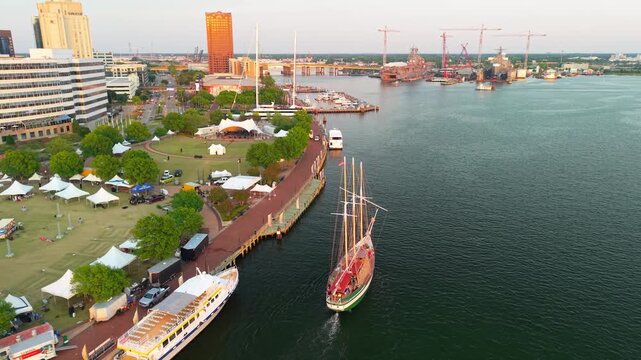 Norfolk, Virginia, beautiful 4K aerial drone video flying over the Elizabeth River toward Town Point Park during a sunset festival, showcasing a large three-masted schooner sailing along the waterfron