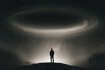 Fototapeta premium Silhouette of a solitary person standing on a hill under a swirling galaxy and starry night sky.