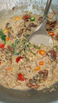 Close-up shot of a ladle scooping traditional Thai salted crab coconut milk dip (Lon Pu Khem), enriched with minced pork, herbs, lemongrass, and colorful chilies. Real-time cooking footage.