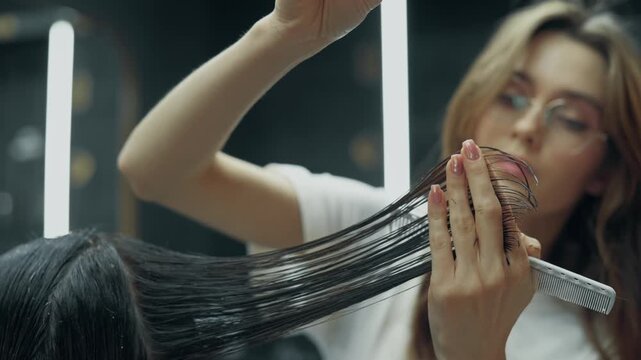 Female barber cutting long wet hair of male client with scissors and comb during professional haircut procedure in modern barbershop