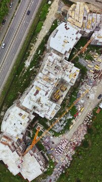 Workers and machines are involved in building a multi-storey structure beside a busy road. Materials are scattered across the site, showing active construction.