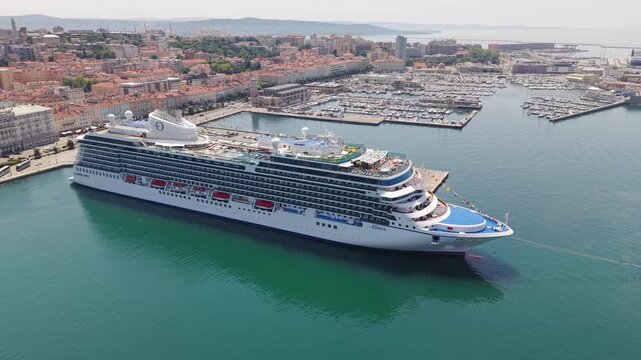 TRIESTE, ITALIA - 9 MAGGIO 2026: Veduta aerea della nave da crociera Oceania Allura ormeggiata alla Stazione Marittima con lo sfondo del panorama cittadino e del colle di San Giusto.