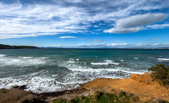 Waves crashing on rocky shore under bright sky near Vouliagmeni in Attica Greece