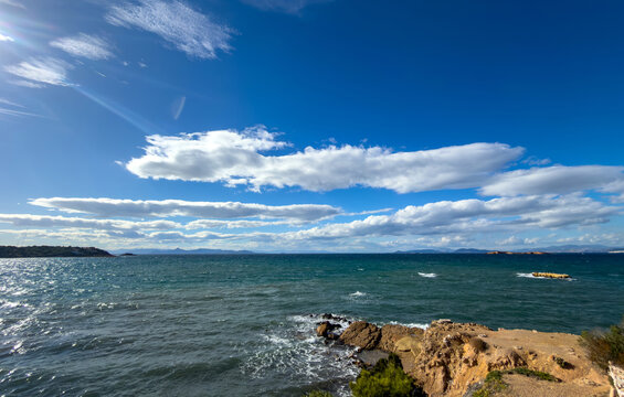 Waves crashing on rocky shore under bright sky near Vouliagmeni in Attica Greece