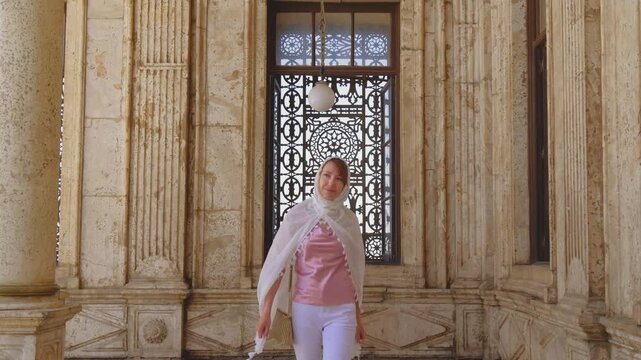 Slow motion shot of female traveler walking toward camera inside historic mosque corridor in Cairo, Egypt. Elegant Islamic architecture and ornate marble details in cinematic 4K travel footage.