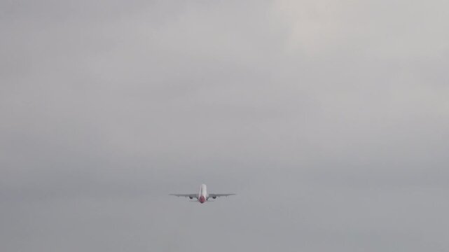 Narrow body jet flying away from camera against a flat gray overcast sky, rear view, small silhouette centered low in frame