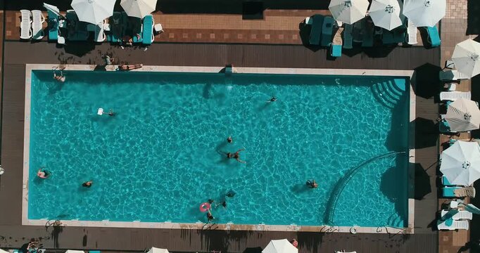 Aerial top down view of a rectangular blue swimming pool surrounded by white umbrellas and sun loungers at a resort