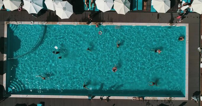 Aerial top down view of a rectangular blue swimming pool surrounded by white umbrellas and sun loungers at a resort