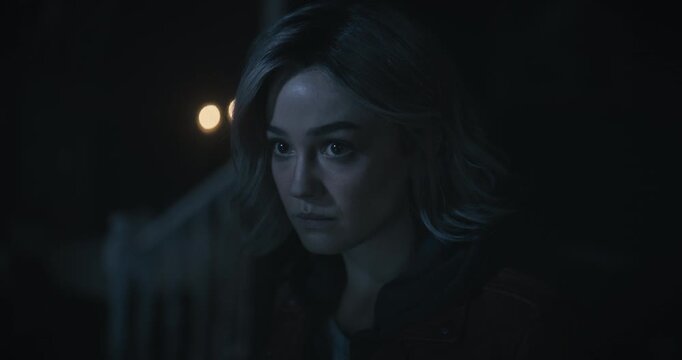 Glistening eyes of serious young woman looking around dark, scary home then down at notebook - tilt, closeup shot