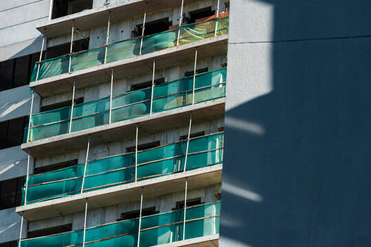 Graphic construction facade layers teal safety mesh with deep urban shadow