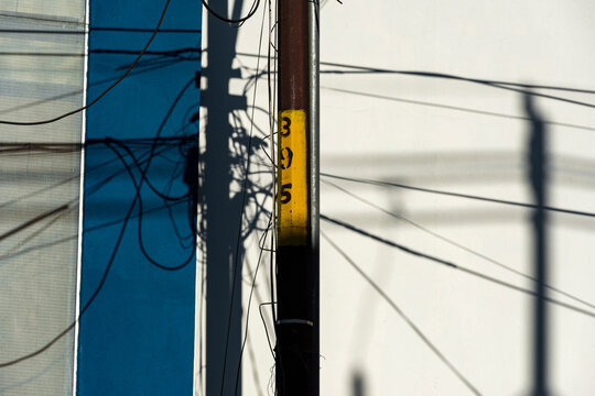Graphic utility pole divides blue wall and white facade with tangled wire shadow