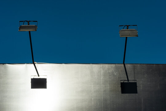 Minimal industrial lights cast twin shadows on silver wall beneath deep blue sky