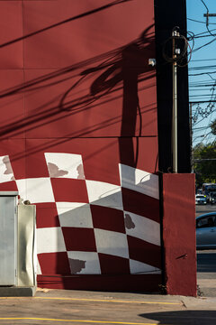 Graphic red wall holds checker pattern and tangled utility shadow at street corner