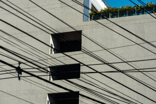 Geometric concrete facade is crossed by dense overhead wire grid and window voids