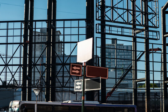 Layered street sign cluster intersects black metal grid and distant city facade