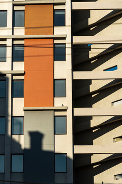 Geometric orange facade aligns window grid with deep stair shadow and warm light