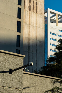 Weathered urban wall layers surveillance arm before stained tower and modern facade