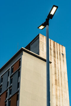 Minimal streetlight stands before stained tower and warm residential facade under blue sky