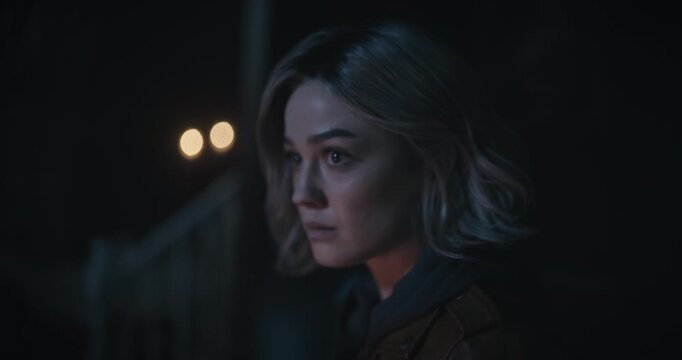 Curious young woman looking around dark, scary home and looking down at her empty hand with flashlight