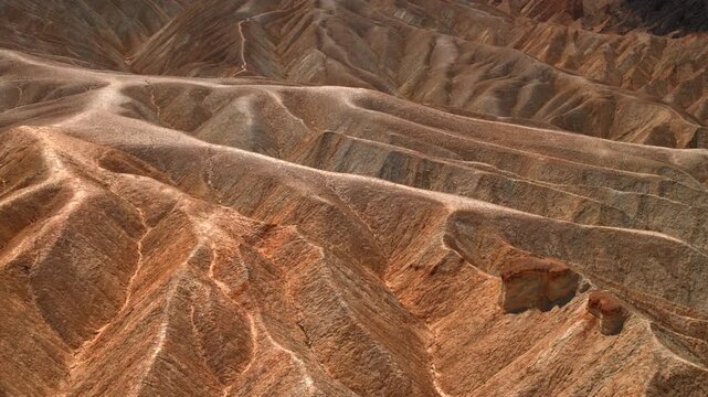 Death Valley National Park Zabriskie Point displays dramatic eroded badlands with colorful sedimentary layers and ridges. Warm golden light illuminates the rugged desert terrain.