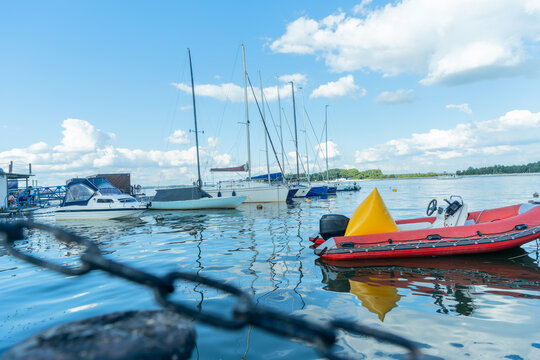 White yachts and powerboats moored at the pier under a blue sky. Beautiful marina harbor with sailing boats and a red inflatable dinghy on a sunny day