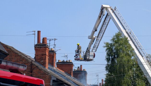 Firefighter in cherry picker platform, crane bucket, hydraulic platform lifting fireman to brick roof chimney during emergency response operation and fire rescue